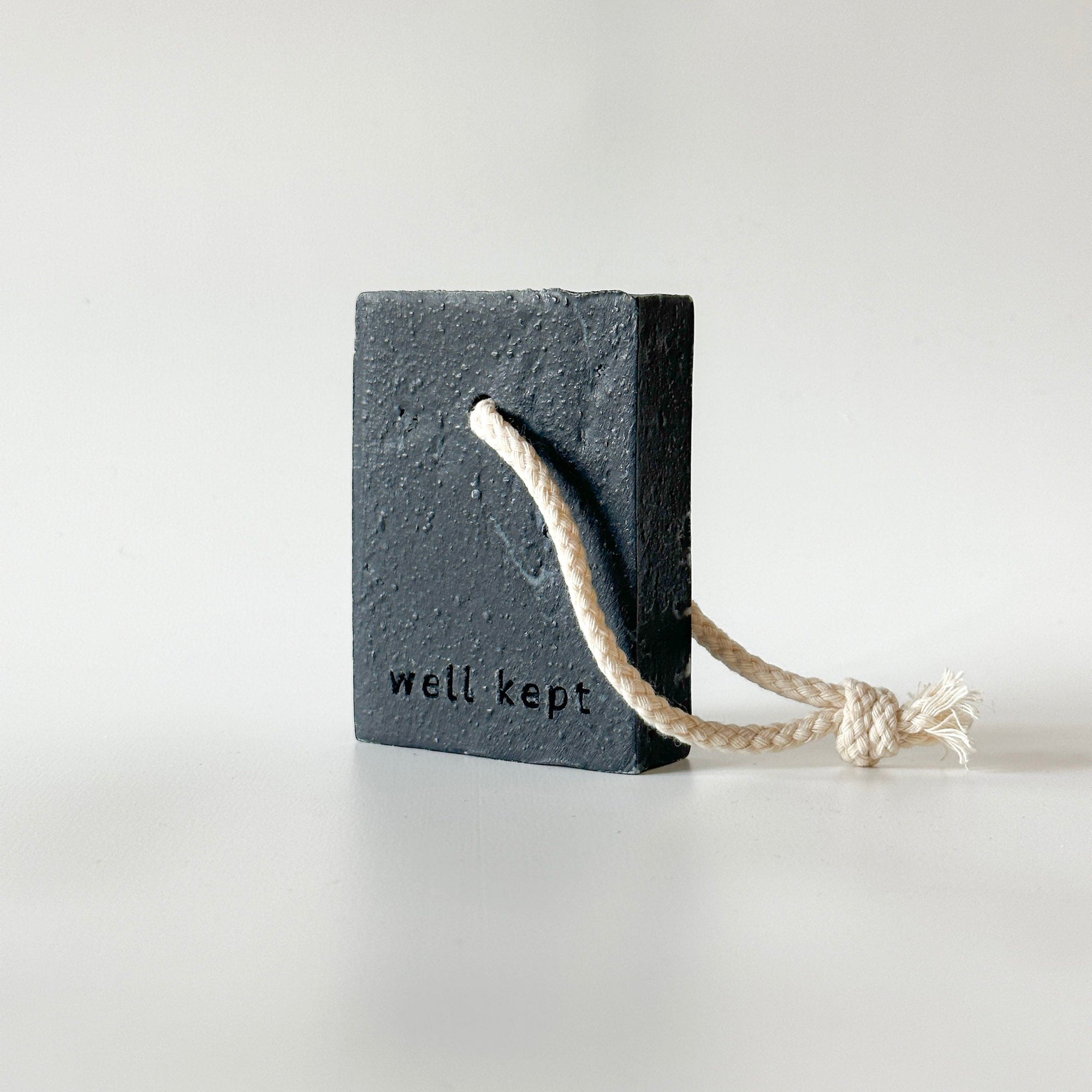 Dark slate soap bar with a natural rope handle and 'well kept' engraving.