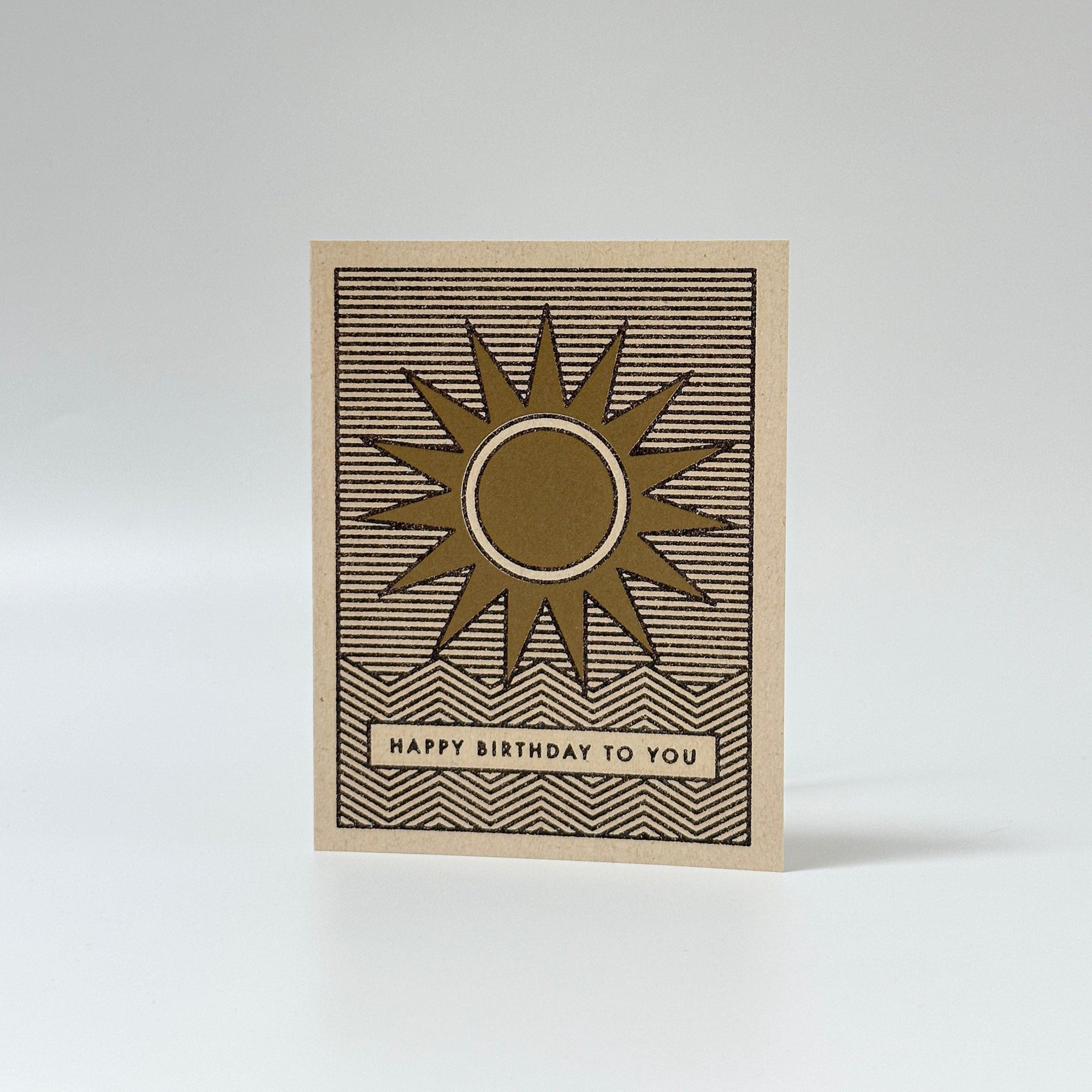 Red Cap Cards premium greeting card featuring brown kraft with a sunburst motif and Happy Birthday to You banner.