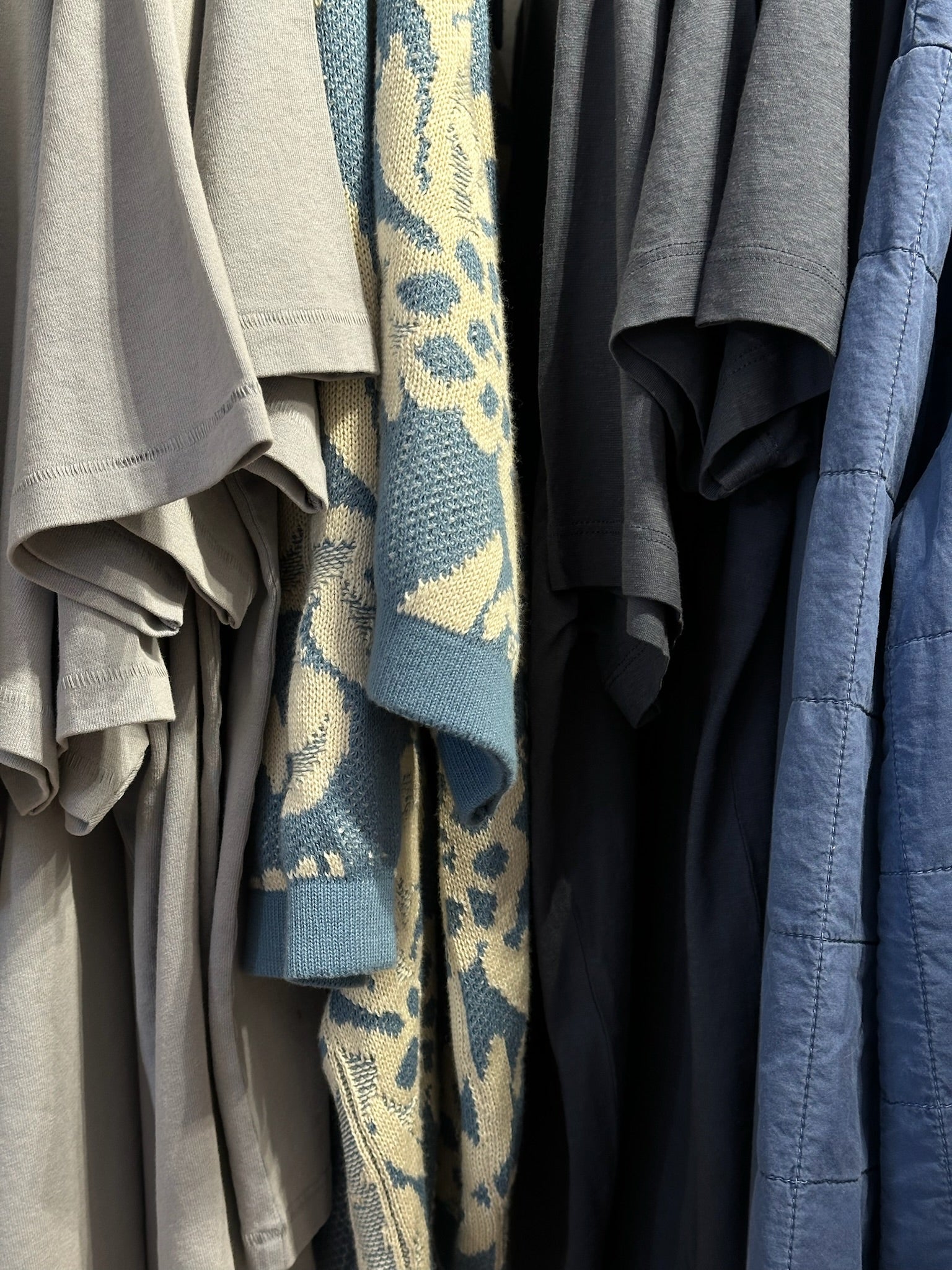 Closet rack with neutral tees and knits, a blue beige patterned knit, and blue outerwear for everyday comfort.