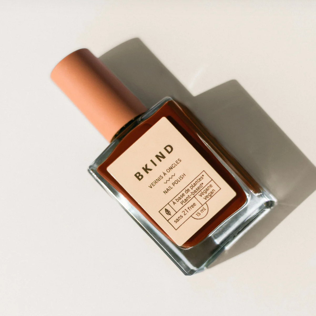 BKIND nail polish bottle with peach cap, vegan formula, featuring natural neutrals and warm amber shades.
