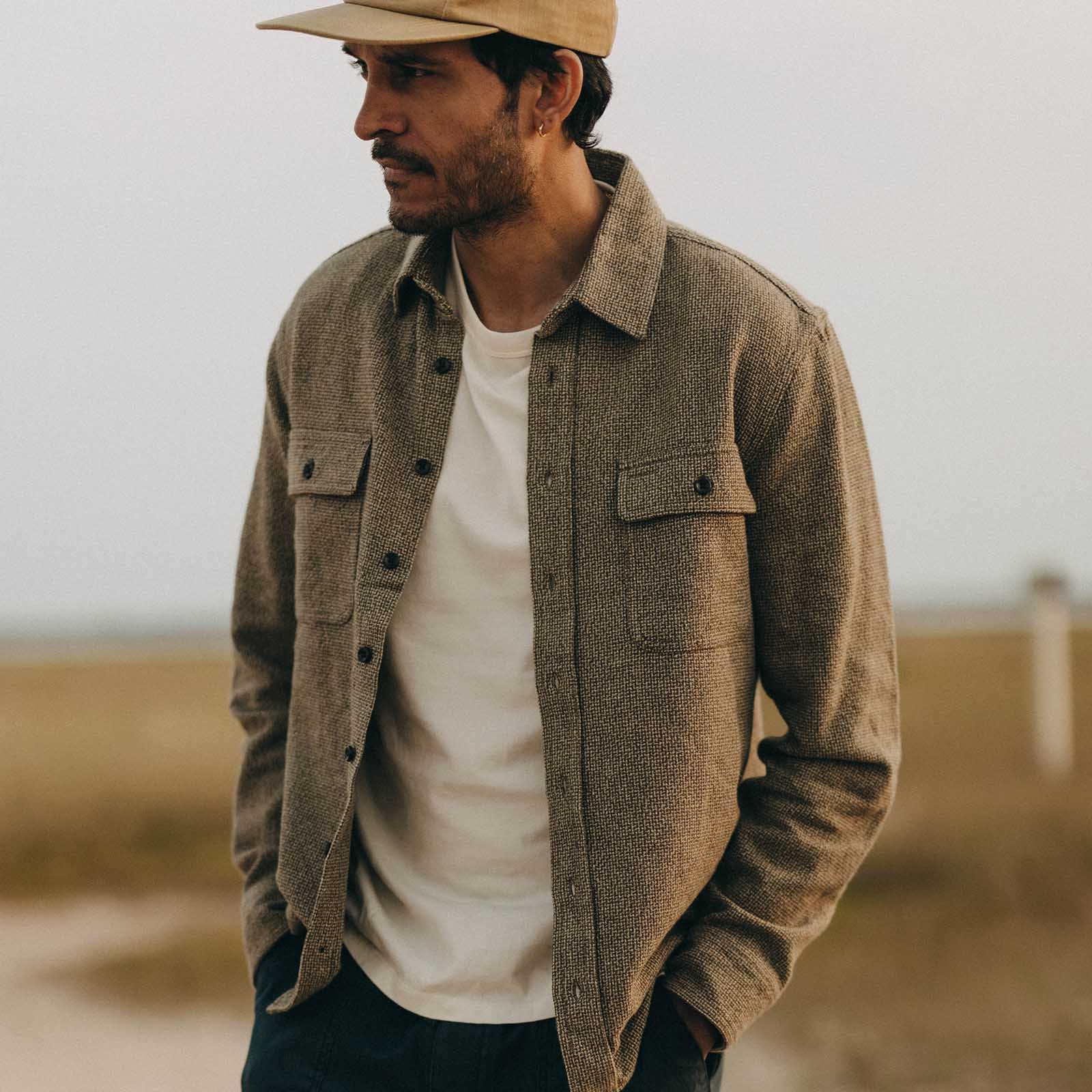 Man wearing a brown jacket and beige cap standing in a field
